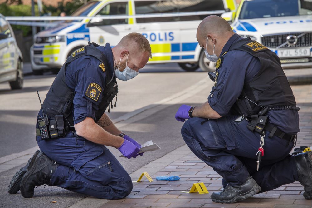 Två uniformsklädda poliser iförda gummihandskar samlar in material från en gata.